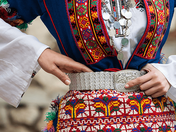 Traditional Bulgarian attire featuring intricate embroidery, vibrant patterns, and a detailed silver belt.