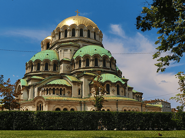 Alexander Nevsky Cathedral in Sofia, Bulgaria, featuring its iconic golden dome and green rooftops against a bright blue sky