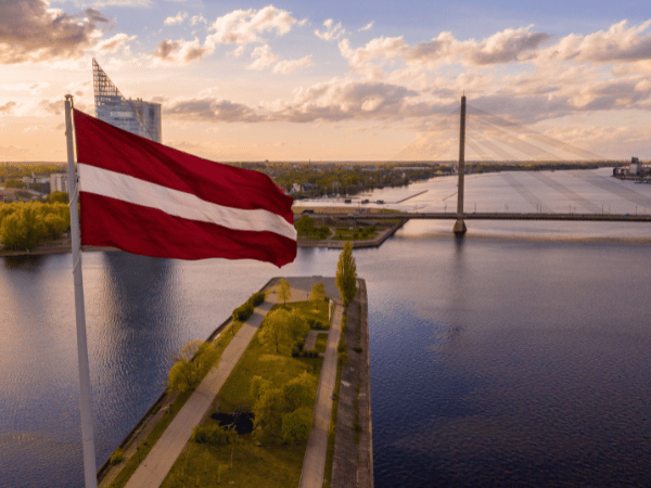 Latvian flag waving over the Daugava River in Riga at sunset – explore Latvia with a top DMC offering tailored travel experiences.