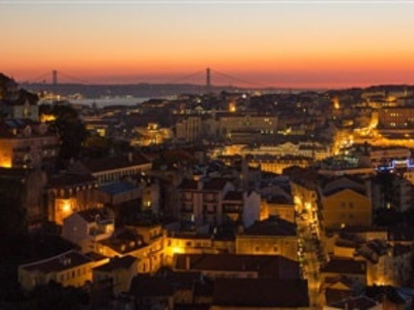 Night view of Lisbon, Portugal, with city lights and the 25 de Abril Bridge in the background.