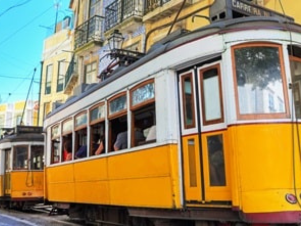 A classic yellow tram climbing a steep street in Lisbon, Portugal, passing historic buildings.