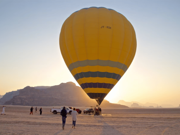 Tourists approaching a large yellow hot air balloon preparing for flight at sunrise in Jordan the desert.