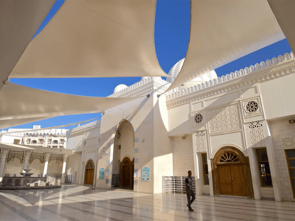 Man walking through the sunlit courtyard of a modern mosque with elegant arches and ornate design in Jordan.