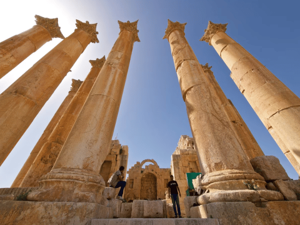 Visitors ascending steps between towering ancient Corinthian columns at a historical site in Jordan